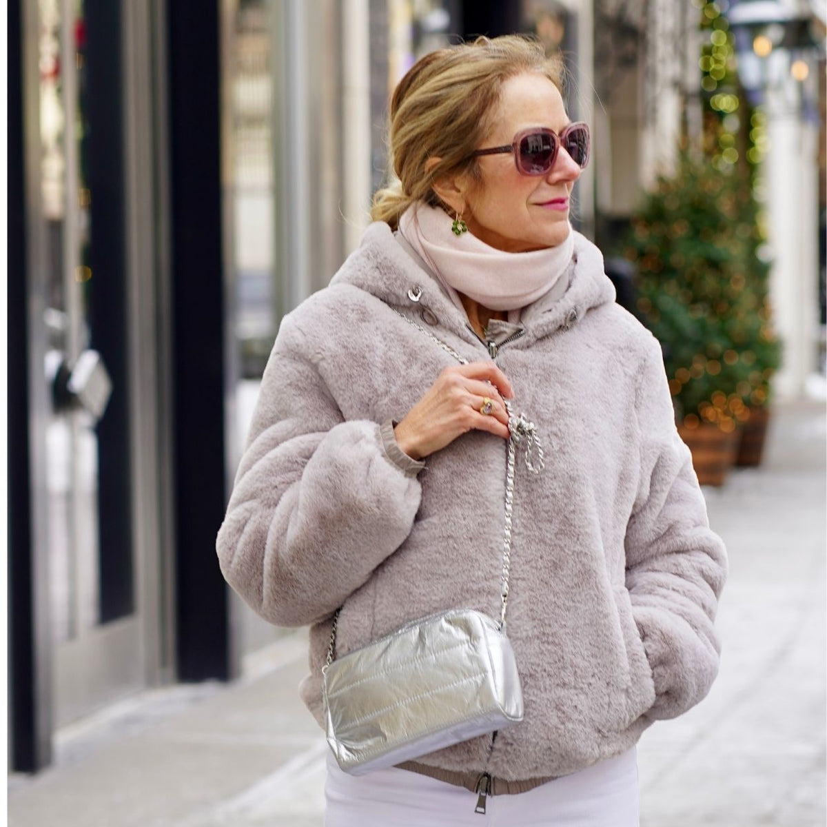 Woman in a light gray faux fur jacket carrying a mini silver puffer purse with a chain strap.