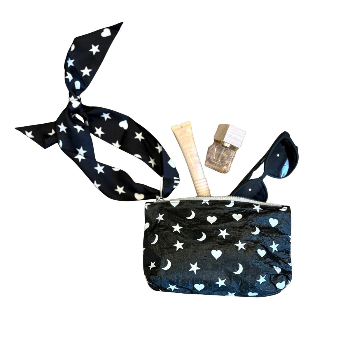 A black zippered pouch with a matching silk tie strap, decorated with a white star and moon pattern, shown with cosmetic items inside on a plain white background.