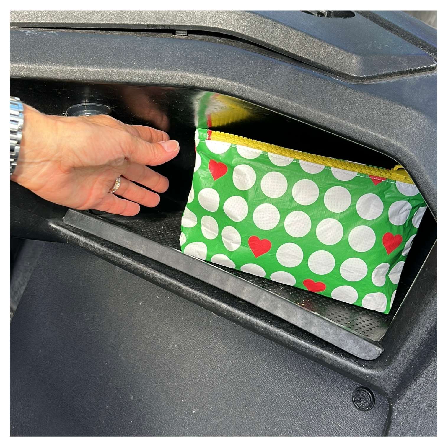 Hand placing a green pouch with white golf balls and red hearts into a golf cart.