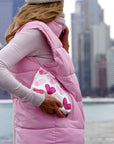 Woman carrying clutch with pink heart print in city.
