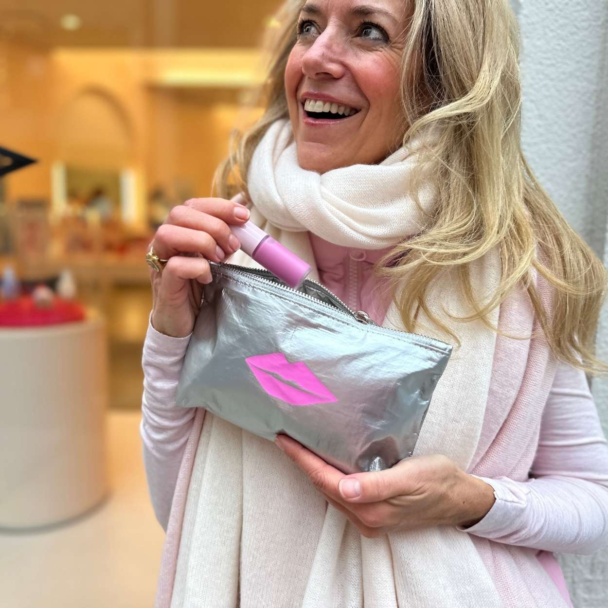 Woman holding a silver pouch with pink lip print in a store setting