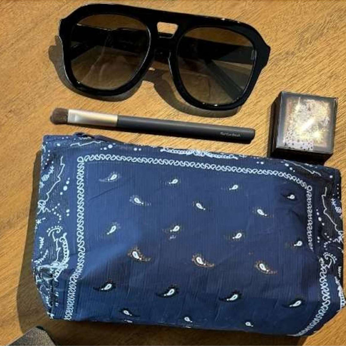 Mini Zipper Pouch Navy Blue Bandana Print with Sunglasses, makeup brush, and compact on a wooden surface.