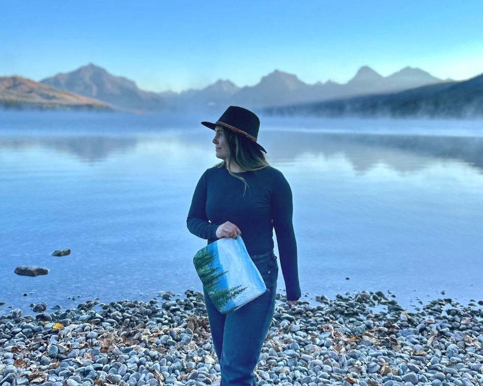 Woman in all black holding pouch by mountains and lake
