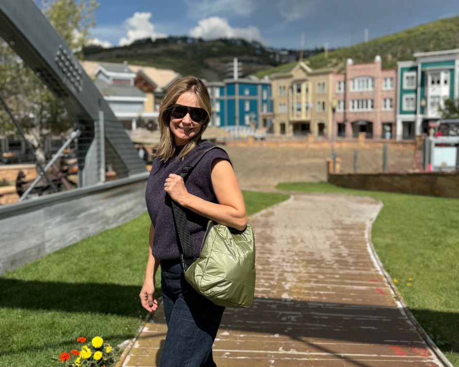 Woman wearing all black carrying green backpack with colorful buildings in background