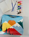 Colorful pouch with mountain design, paint brushes, and paint tubes on a white background