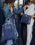 Two women holding blue bandana patterned tote bags against a navy blue door 