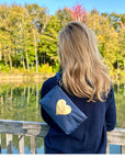 Woman wearing a navy blue wristlet with gold heart overlooking a lake and fall foliage
