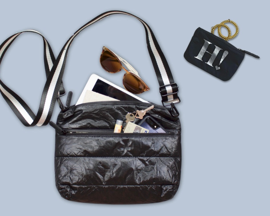 Shimmer black puffer purse with black and white stripe strap, phone, keys, iPad, sunglasses and black card pouch on blue background