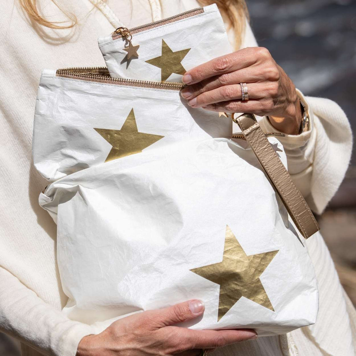 A person outdoors holding several white-colored pouches with metallic gold star patterns.