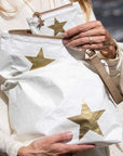 A person outdoors holding several white-colored pouches with metallic gold star patterns.