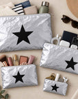 Set of four silver with black star travel pouches with various beauty items and travel essentials on beige background