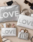 Set of four silver and white travel pouches with LOVE text on beige background displaying beauty and travel items
