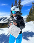 Skier on top of snow capped mountain holding a skier patterned zipper pouch