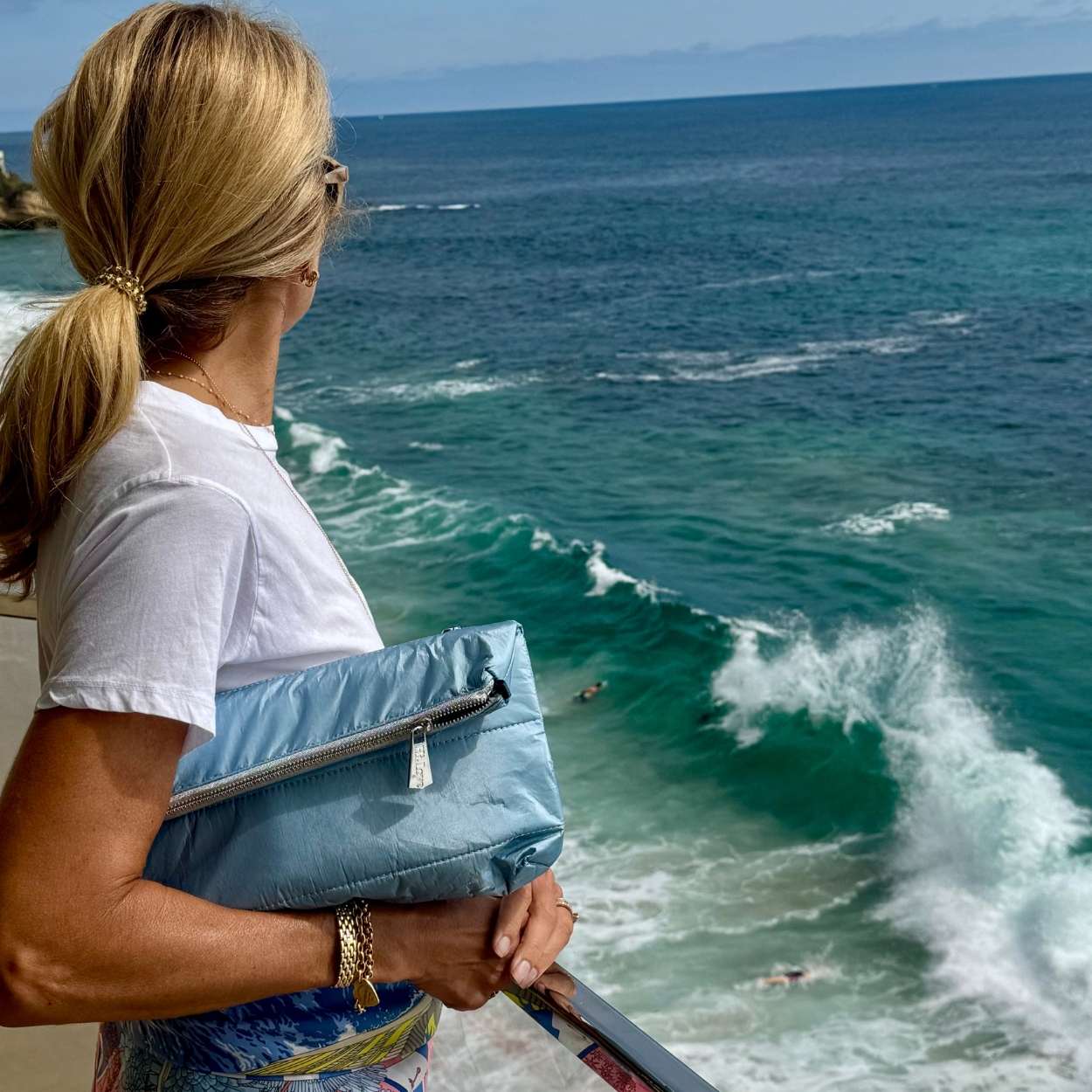 Woman by water hold puffer clutch in shimmer light blue