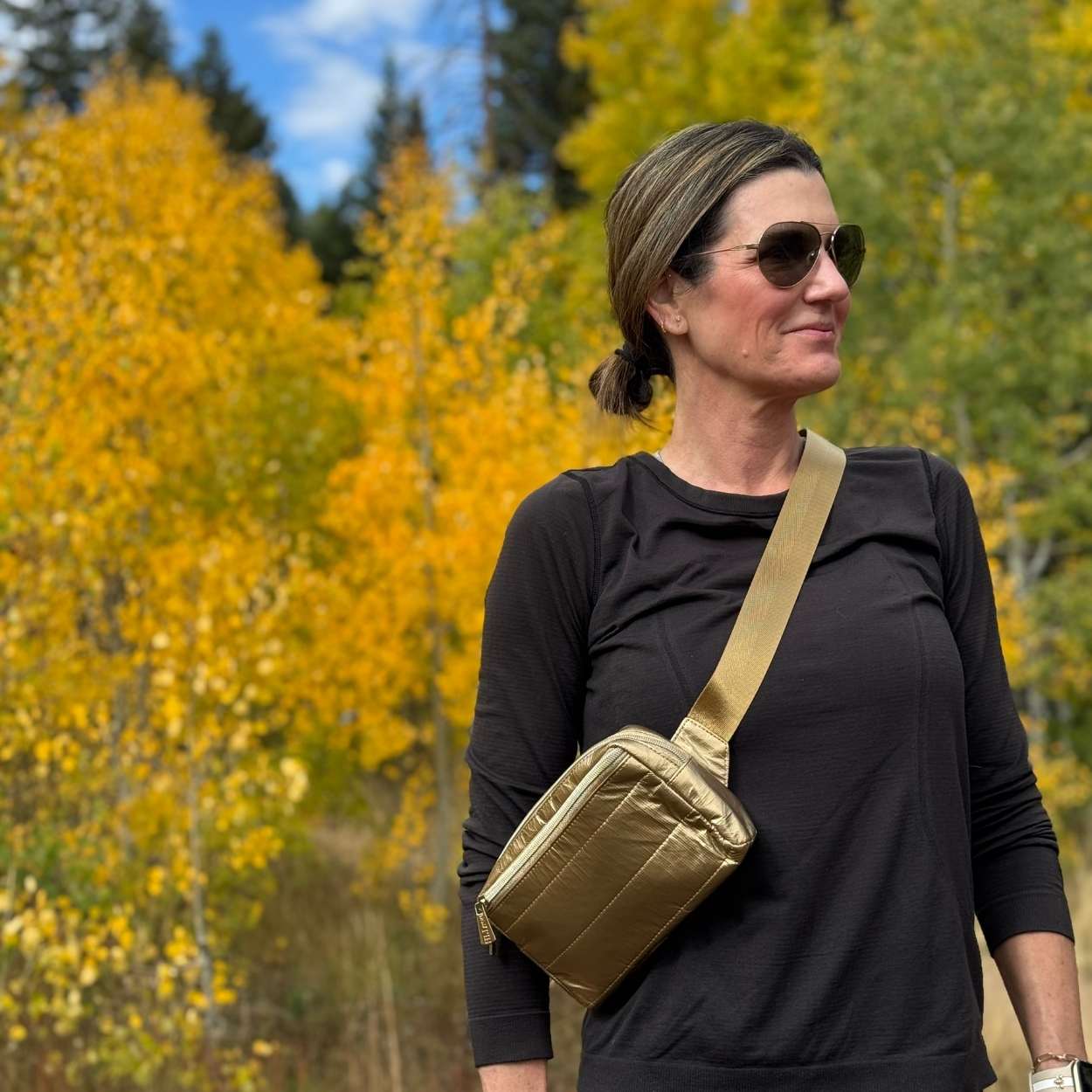 Women standing in nature carry puffer crossbody fanny pack belt bag in gold