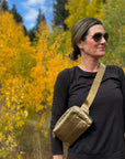 Women standing in nature carry puffer crossbody fanny pack belt bag in gold