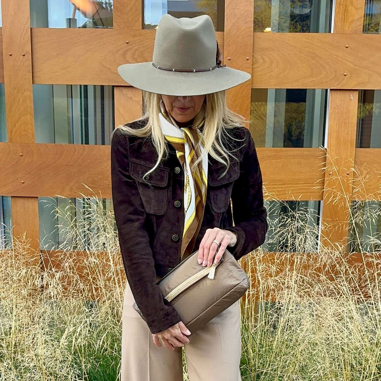 Woman outdoors holding bronze puffer purse clutch and wearing western hat