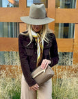 Woman outdoors holding bronze puffer purse clutch and wearing western hat