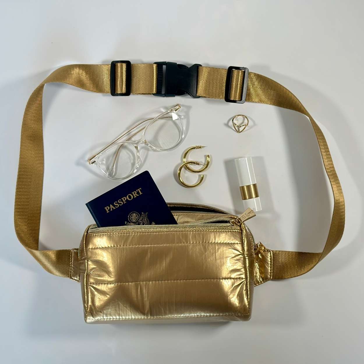 Puffer fanny pack belt bag in gold with travel accessories on white