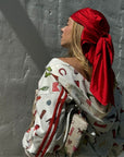 Woman wearing a western print zip up sweatshirt with a Red Silk head scarf standing against a white wall.