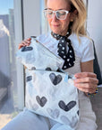Woman in all white outfit holding Set of Two Zip Pouches Language of Love Black and White Heart Print with city background