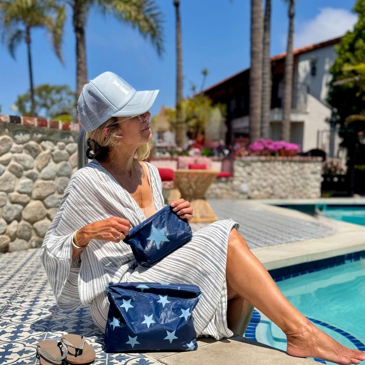 Woman by pool holding set of two zipper pouches in shimmer navy with light blue stars