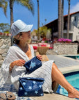 Woman by pool holding set of two zipper pouches in shimmer navy with light blue stars