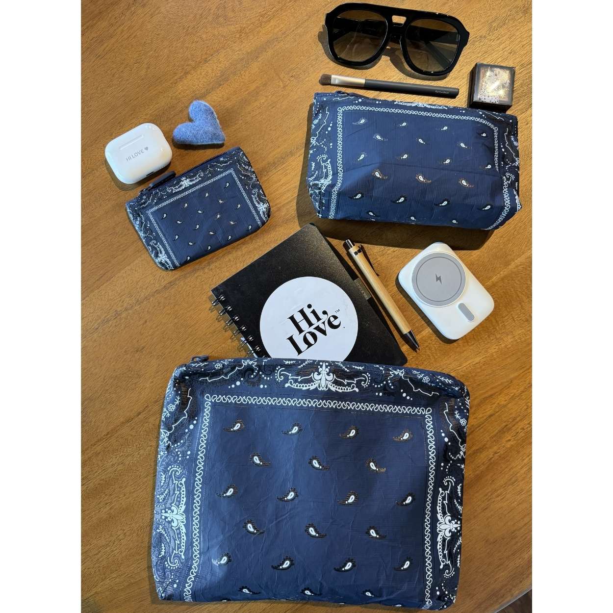 Collection of items including blue bandana-patterned pouches, sunglasses, and small electronic devices on a wooden surface.