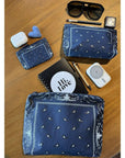 Collection of items including blue bandana-patterned pouches, sunglasses, and small electronic devices on a wooden surface.