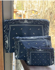 Set of three navy blue Bandana patterned pouches on a wooden surface with a window view.