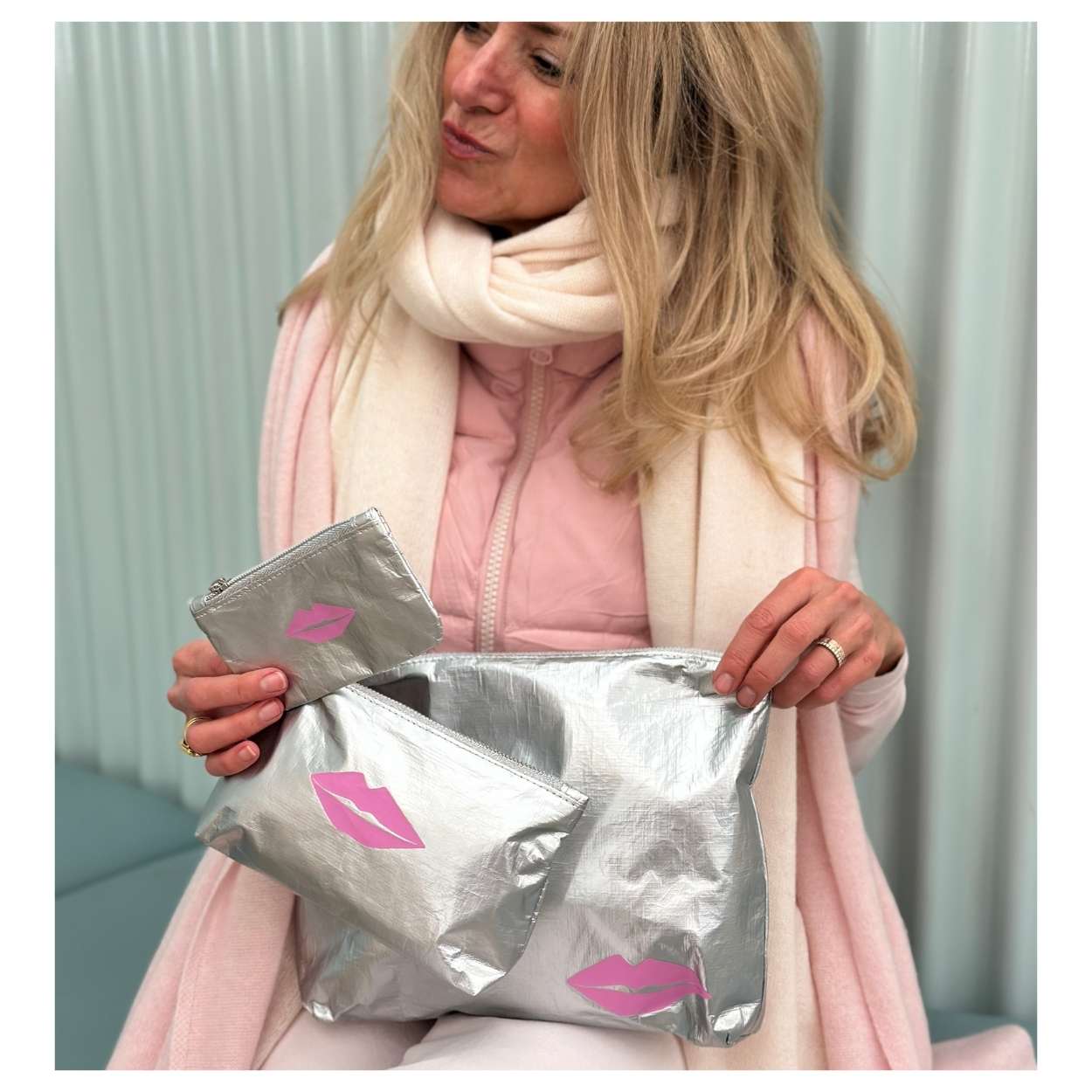 Woman holding a set of three silver pouches with pink lip prints against a light background