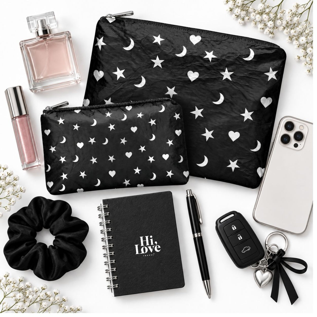Set of Two Zipper Pouches in Black with Heart Moon Star Print with phone, keys, lip balm, notepad, scrunchie and perfume on white background