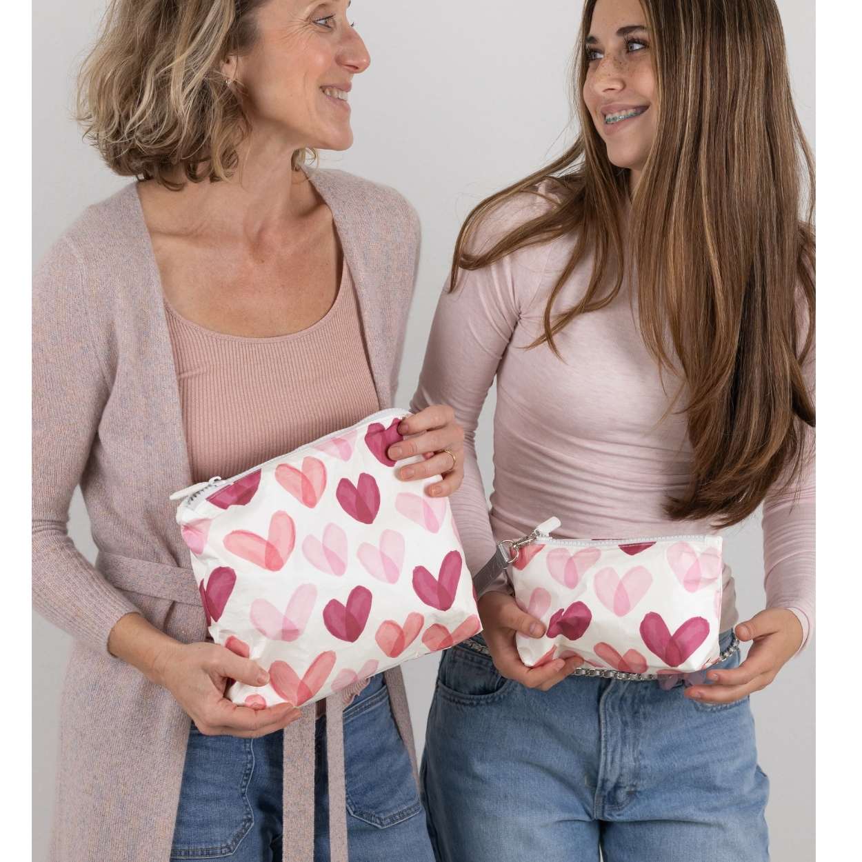 Two women holding pink pouches with heart patterns against a plain background