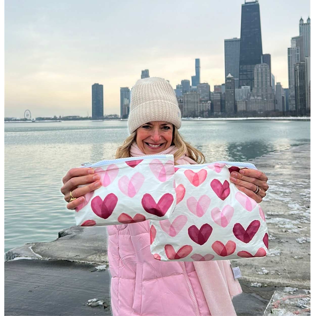 Woman carrying two zipper pouches with heart print with city skyline behind her.