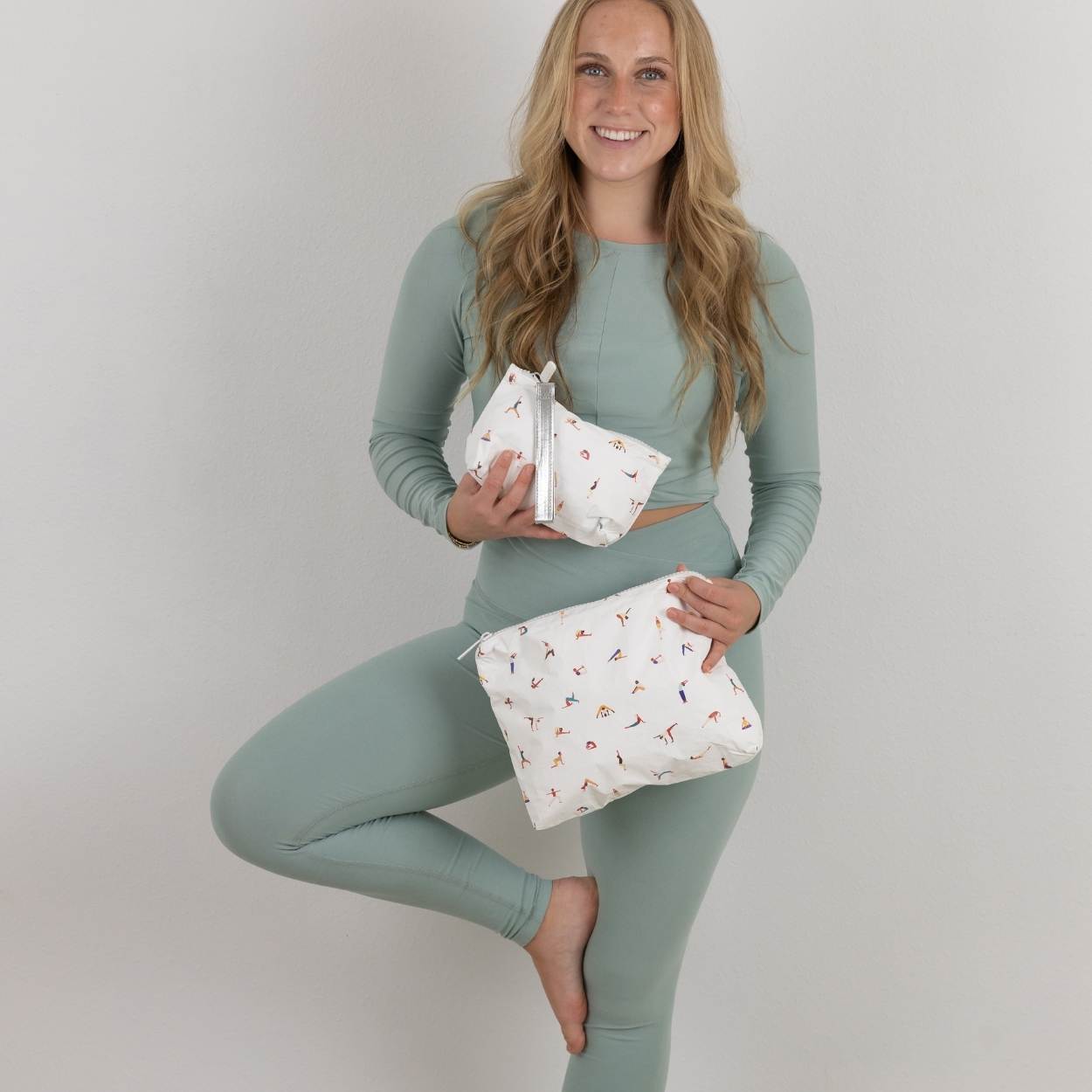 Woman in green athletic wear holding two yoga print pouches against a plain background