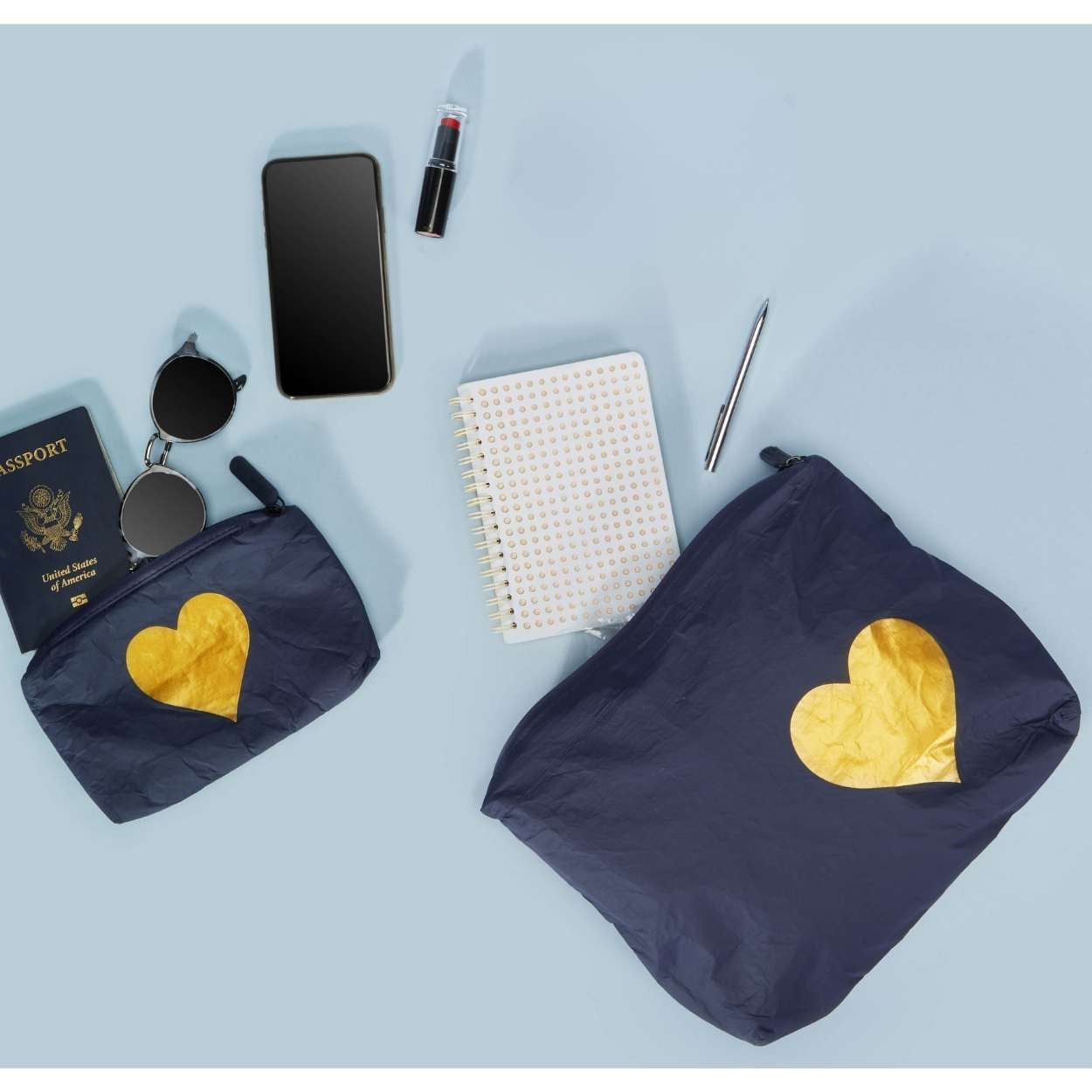 Two navy pouches with heart of Gold emblem, passport, phone, lipstick, notebook, pen on a light blue background