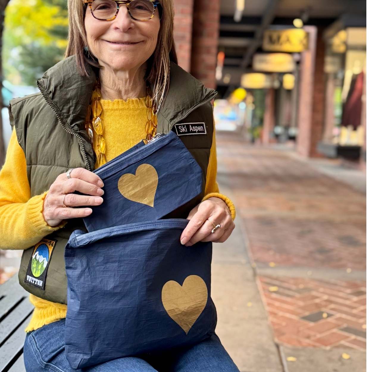 Woman holding two blue bags with gold hearts on a sidewalk