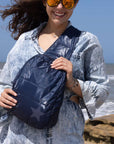 Woman at the beach holding crossbody backpack in shimmer navy with tonal star