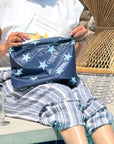 Person sitting by pool holding medium zipper pouch in shimmer navy with light blue stars