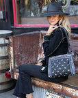 Woman in black hat sitting on bench holding crossbody purse in black bandana print