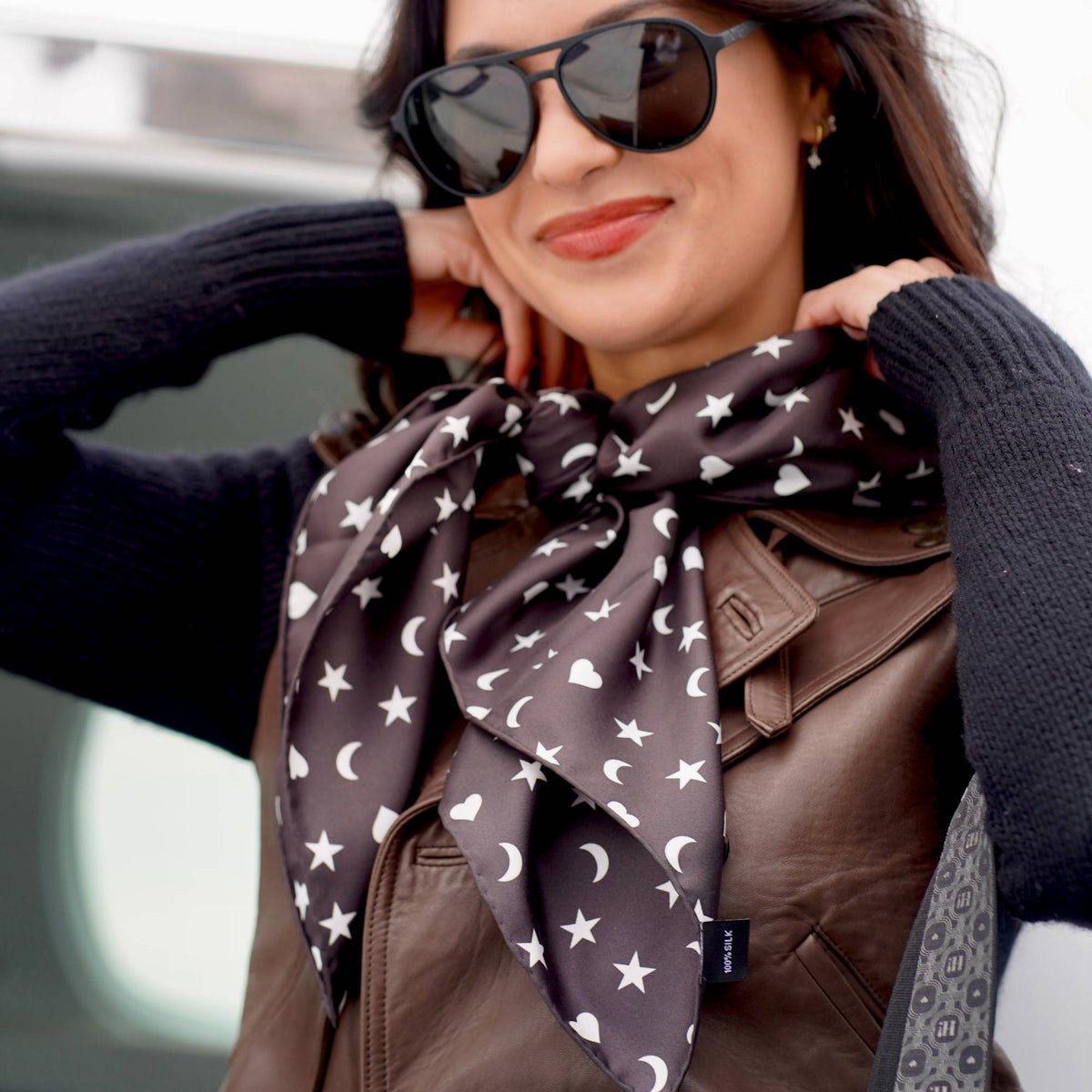 Woman wearing Signature Silk Scarf in black with white hearts, moons, and stars tied around the neck