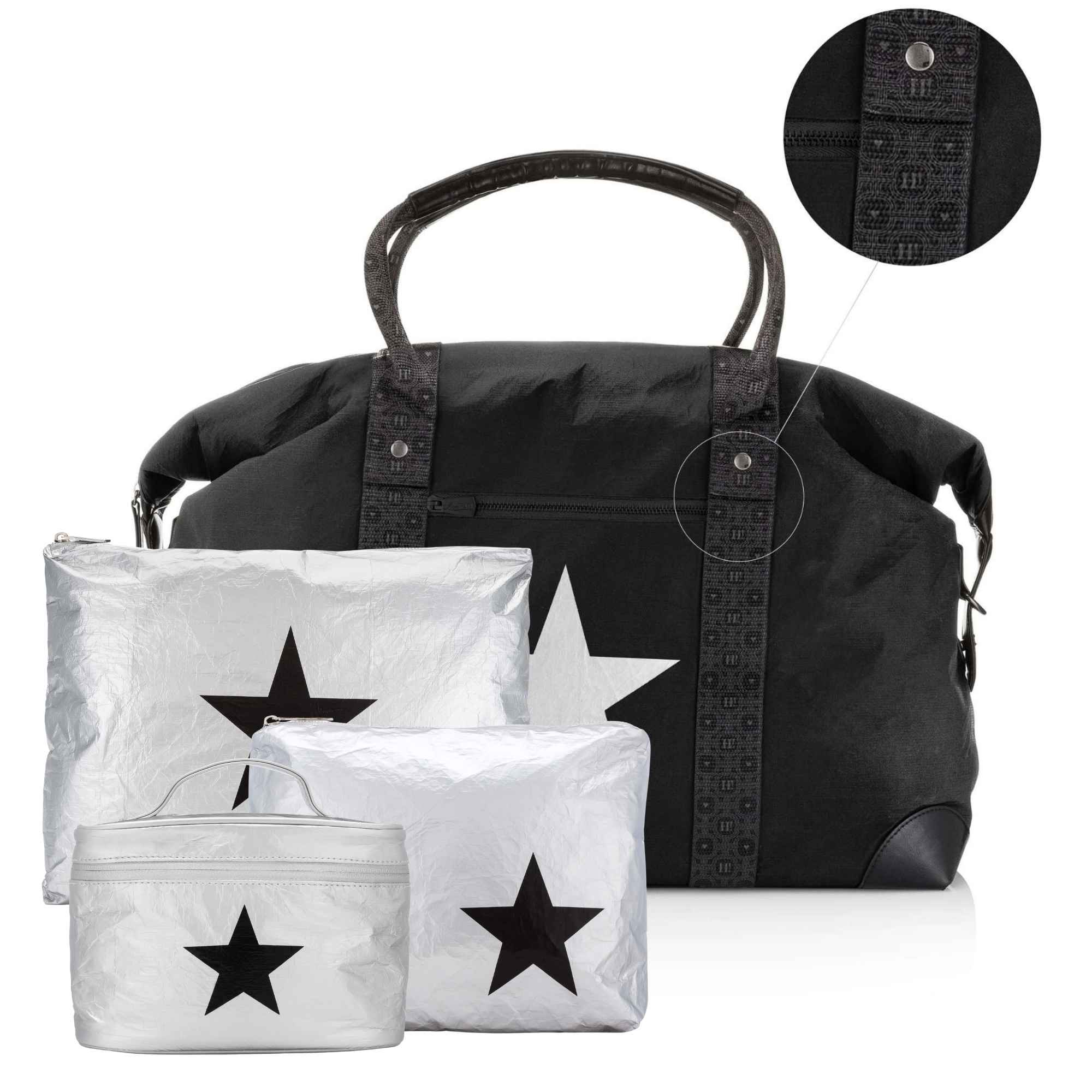 A black duffel bag with signature patterned straps, shown with three matching silver packing cubes featuring black star prints. A circular inset at the top right shows a close-up of the strap hardware and fabric detail.