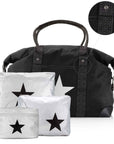 A black duffel bag with signature patterned straps, shown with three matching silver packing cubes featuring black star prints. A circular inset at the top right shows a close-up of the strap hardware and fabric detail.