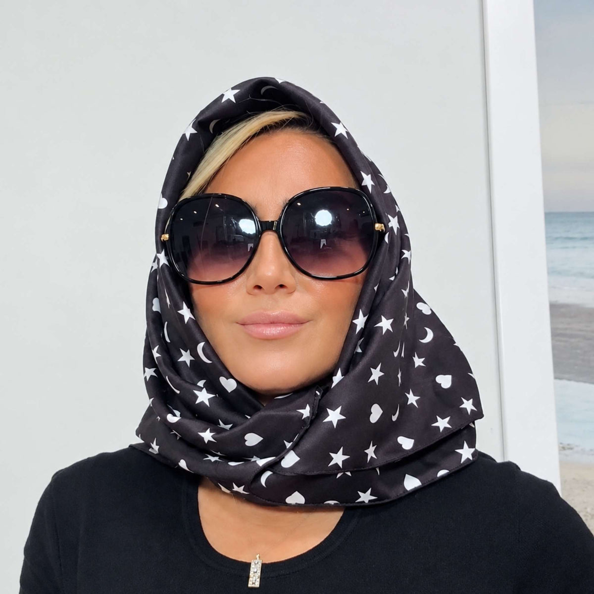 Model wearing the black Signature scarf with white hearts, moons and stars wrapped around her head like a hood.