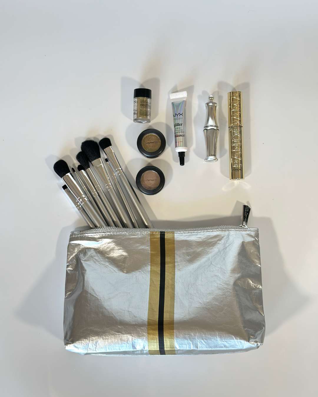 Makeup set with a gold and silver stripe zipper pouch on a white background