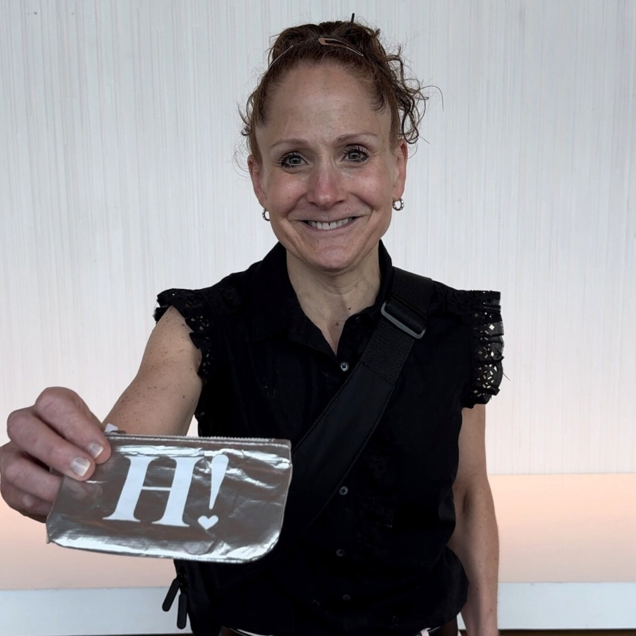 Woman smiling holding silver card pouch with white H!