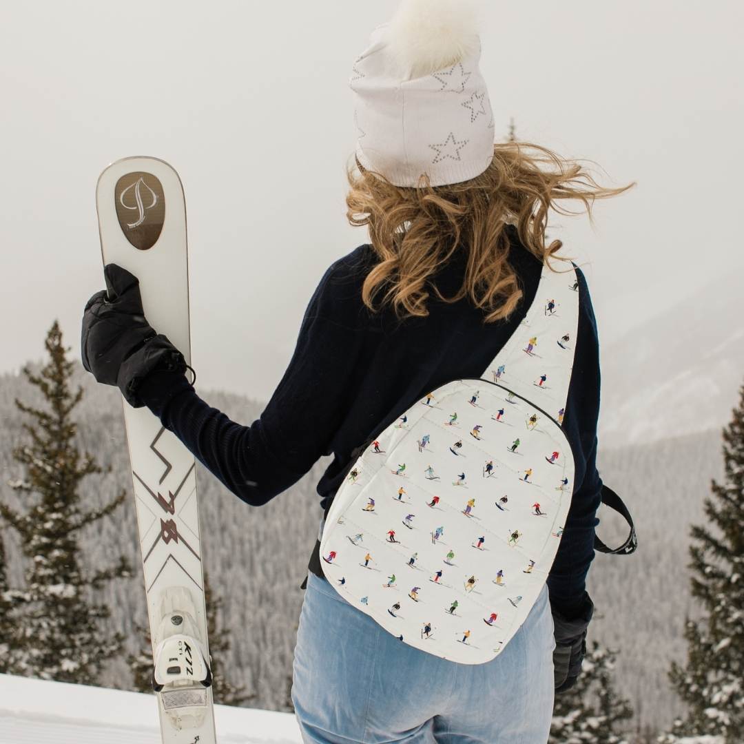 Person holding skis and wearing a skier patterned backpack in a snowy landscape