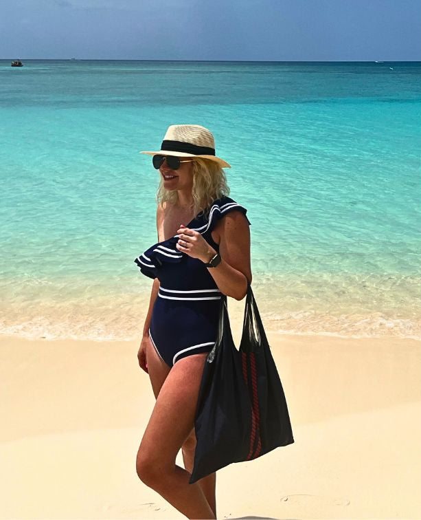 Woman standing by the ocean holding a navy with red rope stripe tote
