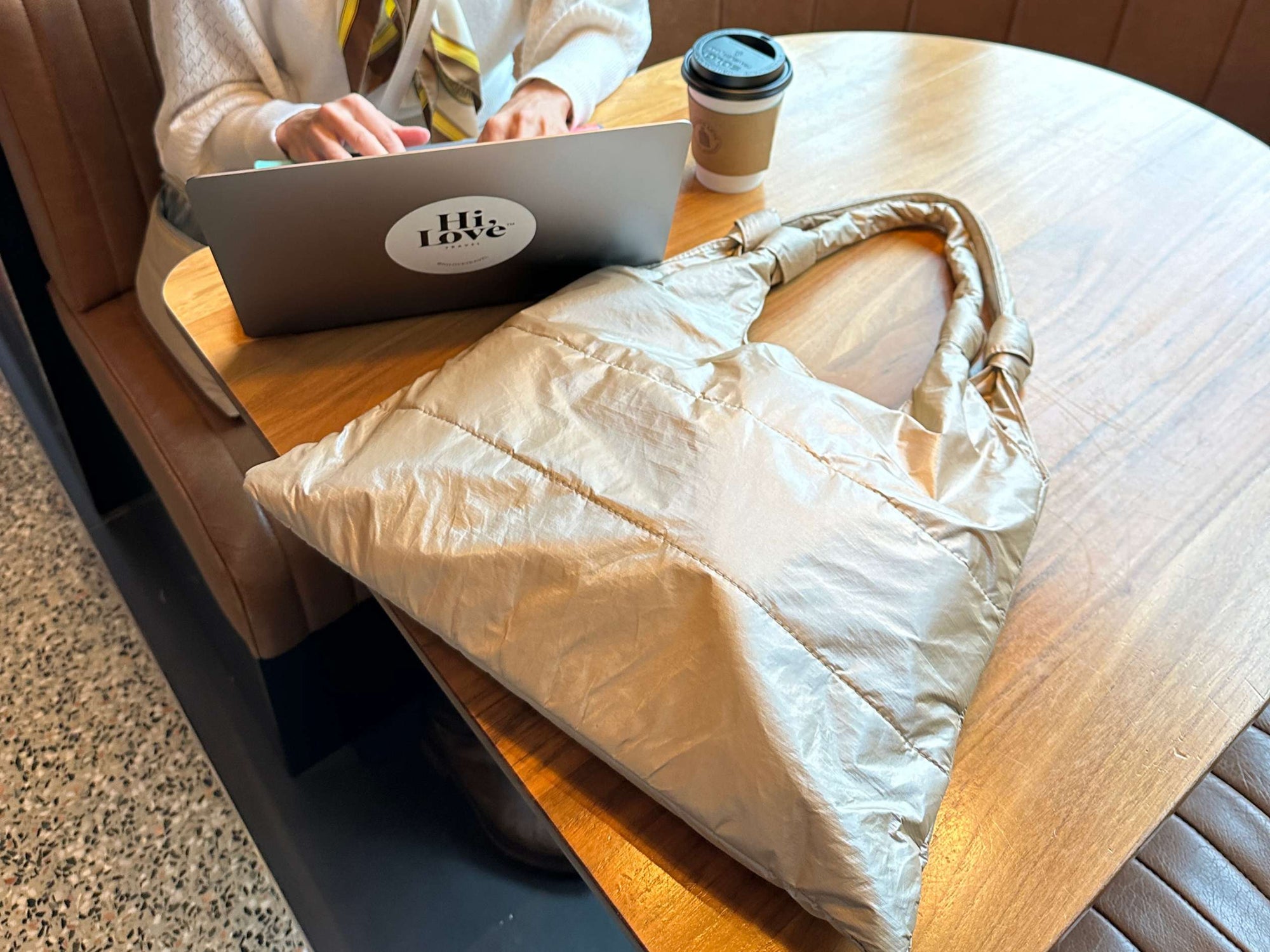 Person using a laptop with a 'Hi Love' sticker on a wooden table, next to a beige tote bag.