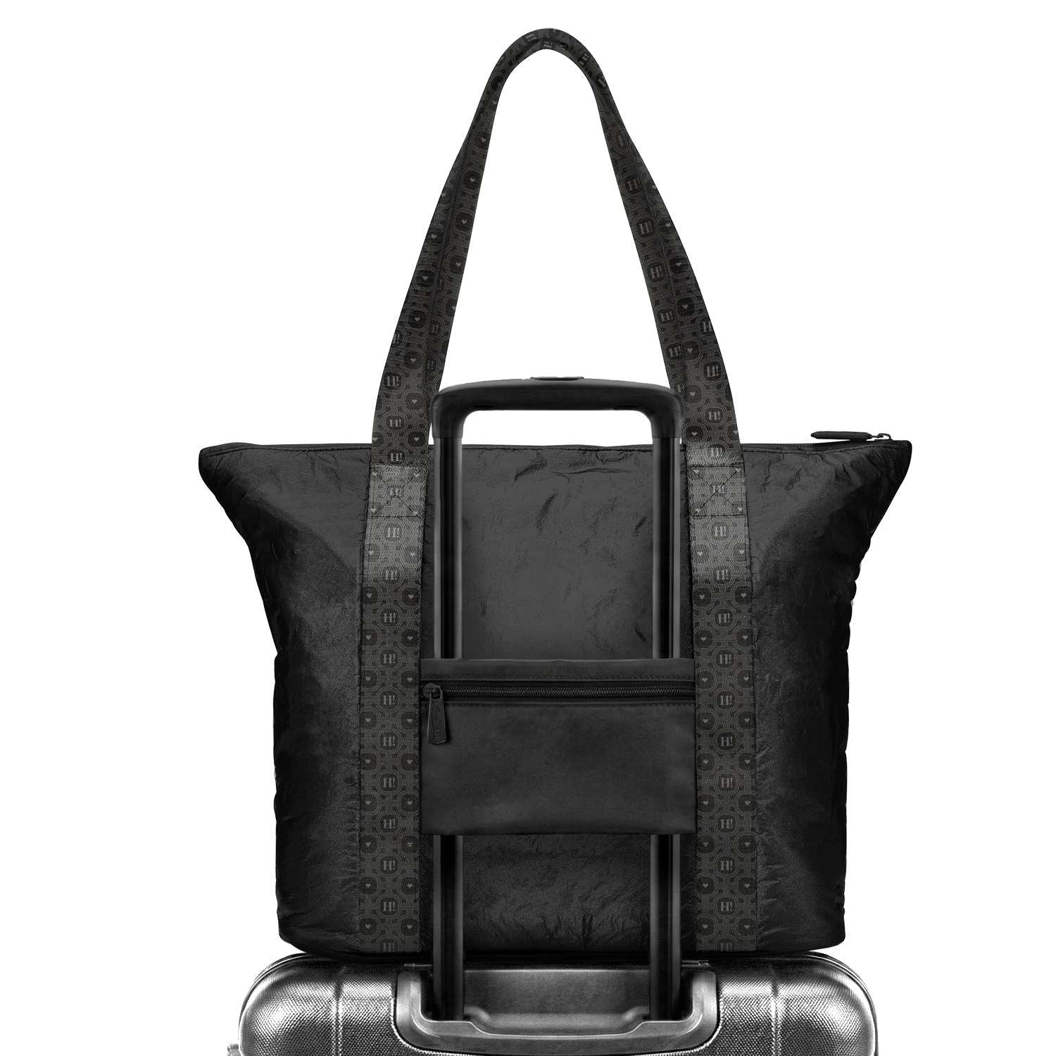 A black expandable rolling suitcase bag  with trolley sleeve with patterned straps, shown with its telescoping handle extended and resting on top of a silver suitcase against a white background.